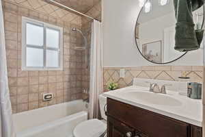 Bathroom featuring vanity, shower / bath combination with curtain, tile walls, and a wainscoted wall