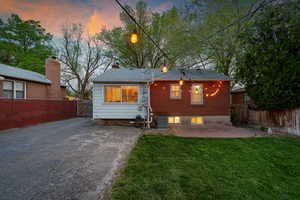 Back of property at dusk with a patio area, a fenced backyard, asphalt driveway, and a gate