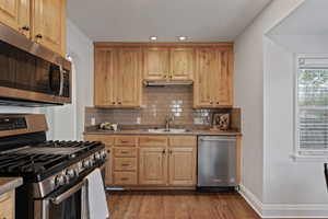 Kitchen with stainless steel appliances, light wood finish cabinetry, dark wood-style flooring, recessed lighting, and decorative backsplash