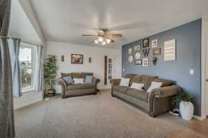 Carpeted living area with a ceiling fan and baseboards