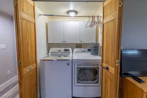 Laundry room with a textured ceiling, independent washer and dryer, cabinet space, and wood finished floors
