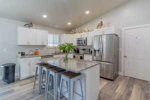 Kitchen with stainless steel appliances, a kitchen bar, light stone counters, white cabinets, and light wood finished floors