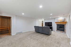 Living room featuring a tiled fireplace, light colored carpet, recessed lighting, open door to storage area, and basement entrance