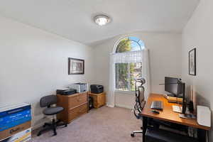 Office/Bedroom space featuring a partial vaulted ceiling and arched window, light carpet, and baseboards