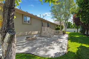 Rear view of house featuring stucco siding, basement entrance, and a patio area