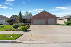 Single story home featuring an attached garage, brick siding, driveway, and a front lawn