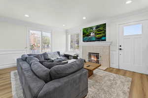 Living area with light wood-style floors, crown molding, a fireplace, recessed lighting, and wainscoting