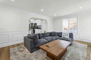 Living room featuring arched walkways, wood finished floors, a decorative wall, ornamental molding, and wainscoting