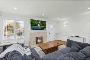 Living area featuring a decorative wall, wood finished floors, a wainscoted wall, a tiled fireplace, and crown molding