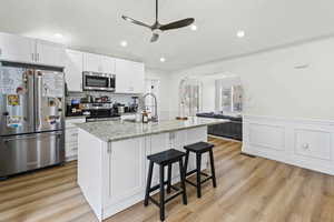 Kitchen with stainless steel appliances, arched walkways, a ceiling fan, white cabinetry, and a kitchen bar