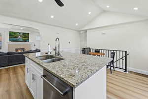 Kitchen with a warm lit fireplace, light stone countertops, white cabinetry, a center island with sink, and light wood finished floors