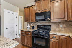 Kitchen with black appliances, decorative backsplash, wood finish cabinetry, and dark wood-style flooring