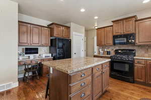 Kitchen with black appliances, wood finish cabinetry, backsplash, a kitchen island, and recessed lighting