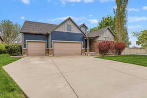 Craftsman-style house featuring board and batten siding, a front yard, driveway, stone siding, and a garage