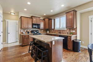 Kitchen with wood finish cabinets, light wood-style floors, black appliances, a breakfast bar area, and recessed lighting