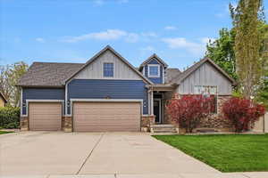 Craftsman house featuring board and batten siding, concrete driveway, stone siding, an attached garage, and a front lawn