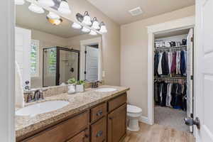 Primary Bathroom featuring double vanity, a stall shower, a walk in closet, and light wood-type flooring