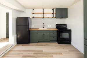 Kitchen with black appliances, open shelves, decorative backsplash, light wood-style floors, and green cabinets
