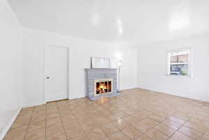 Unfurnished living room featuring a warm lit fireplace and light tile patterned floors