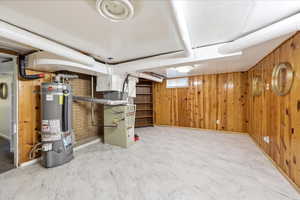 Finished basement featuring wood walls, secured water heater, and heating unit
