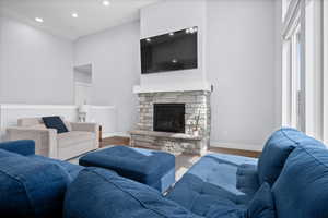 Living room featuring wood finished floors, a cathedral ceiling, a stone fireplace, and recessed lighting