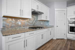 Kitchen featuring white cabinetry, light stone countertops, stainless steel appliances, and dark wood finished floors