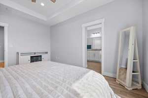 Bedroom featuring light wood-style flooring, a tray ceiling, recessed lighting, a ceiling fan, and ensuite bath