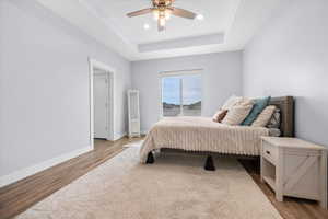 Owners suite with light wood-style floors, a raised ceiling, ceiling fan, and upgraded recessed lighting