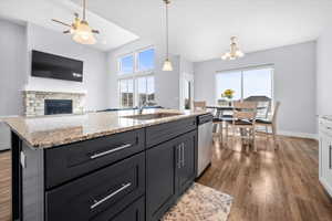 Kitchen with a fireplace, light stone countertops, dark wood finished floors, and a kitchen island with sink