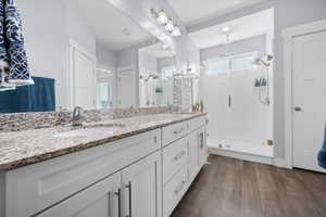 Bathroom featuring double vanity, a stall shower, with rain shower, linen closet, and dark wood finished floors