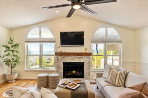 Living area featuring wood finished floors, a ceiling fan, a fireplace, and a textured ceiling