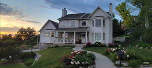View of front facade with a lawn, a chimney, covered porch, and roof with shingles