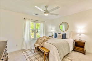 Bedroom with light carpet, ceiling fan, and a textured ceiling