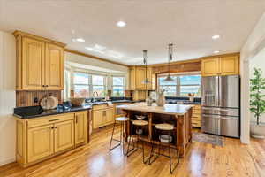 Kitchen featuring stainless steel refrigerator with ice dispenser, hanging light fixtures, light wood finished floors, healthy amount of natural light, and a textured ceiling