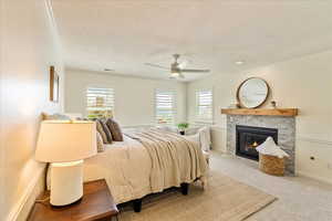 Bedroom featuring carpet flooring, multiple windows, a textured ceiling, a fireplace, and a ceiling fan