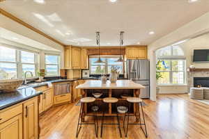 Kitchen with open floor plan, a breakfast bar, stainless steel appliances, light wood-style flooring, and a stone fireplace