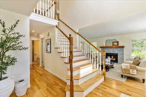 Stairs with wood finished floors and a stone fireplace