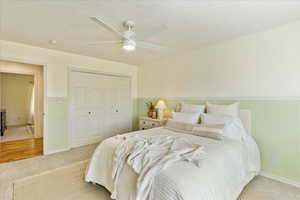 Carpeted bedroom with a wainscoted wall, a closet, ceiling fan, and a textured ceiling
