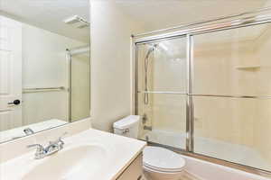 Full bath featuring vanity, a textured ceiling, and shower / bath combination with glass door