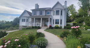 Victorian home with a chimney, a porch, a front yard, and stone siding