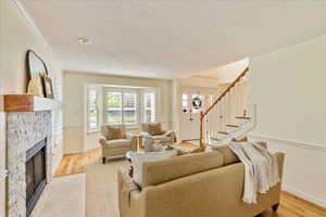 Living area featuring a fireplace, a textured ceiling, light wood-style flooring, and ornamental molding