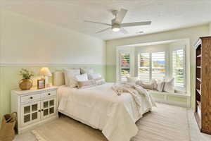 Bedroom featuring light carpet, a textured ceiling, wainscoting, and a ceiling fan