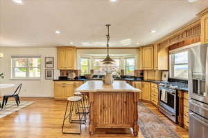 Kitchen featuring a center island, stainless steel appliances, light wood-style flooring, a kitchen bar, and a textured ceiling