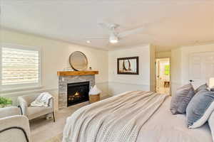 Carpeted bedroom featuring a fireplace, multiple windows, ceiling fan, ensuite bathroom, and a textured ceiling