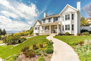 View of front facade with a chimney, covered porch, a front lawn, and stone siding
