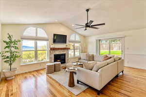 Living room with light wood finished floors, ceiling fan, a textured ceiling, and a stone fireplace