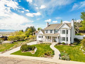 View of front of home with covered porch, a chimney, a front yard, roof with shingles, and stone siding