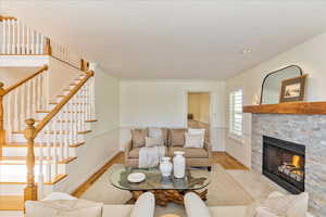Living area with light wood-style floors, a stone fireplace, a textured ceiling, and ornamental molding