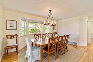 Dining area featuring light wood-style floors, suspended lighting, a textured ceiling, and crown molding