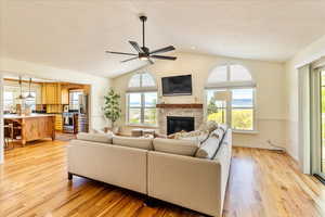 Living room featuring light wood-style flooring, plenty of natural light, a ceiling fan, and a glass covered fireplace
